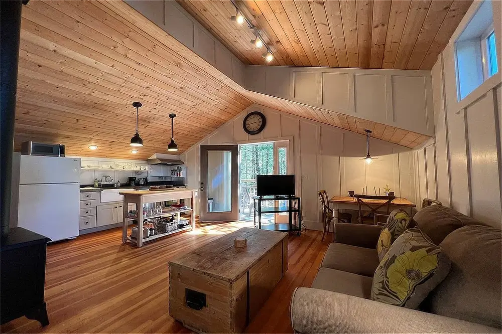 Open-plan living room and kitchen with vaulted wood ceiling, hardwood floors, and comfortable seating.