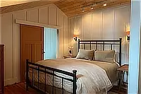 Bedroom with a metal-frame bed, wood ceiling, and bedside lighting.