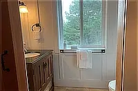 Bathroom vanity and toilet beside a window overlooking greenery.