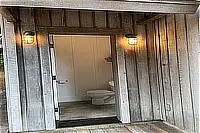Exterior entrance to a small bathroom beneath a covered wooden porch.
