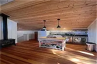 Kitchen island, appliances, and open-plan interior beneath a vaulted wood ceiling.