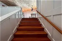 Wooden staircase with white walls and handrail leading to the upper floor.