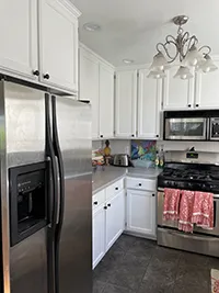 A modern kitchen in this Humboldt Air BnB features white cabinets, a stainless steel refrigerator, and a stainless steel oven with a stove. A microwave is mounted above the stove, and a white chandelier hangs from the ceiling. Red hand towels hang from the oven handle.