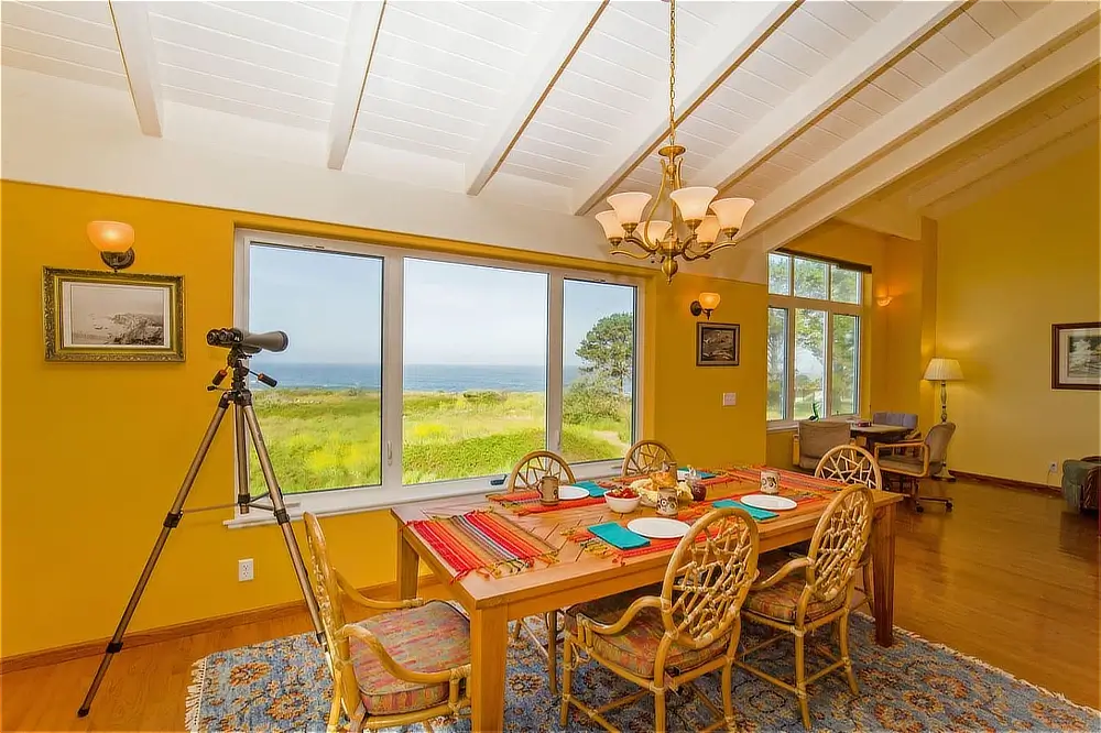 Dining area with colorful table settings, telescope, and large windows overlooking the ocean.