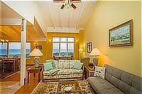 Living room with two sofas, vaulted ceiling, and large windows facing the ocean.