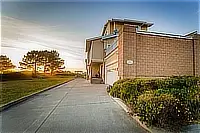Side view of Pelican Point showing the driveway, landscaped shrubs, and coastal surroundings.