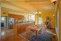 Open dining area and kitchen with wooden cabinetry, colorful table settings, and a telescope near the ocean-facing windows.