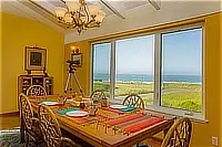 Dining room with a wooden table, wicker chairs, telescope, and expansive ocean views through large windows.