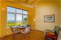 Ocean-view sitting area with a small table, upholstered chairs, and a green armchair.