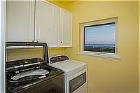 Laundry room with a washer, dryer, white cabinets, and a window overlooking the ocean.