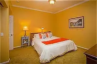 Bedroom with yellow walls, queen bed, white bedding, and orange accent pillows.