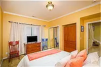 Bedroom with queen bed, wooden dresser, television, and yellow walls.