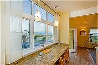 Granite breakfast counter beside tall windows overlooking the ocean, with pendant lights overhead.