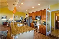 Open kitchen with granite breakfast bar, wooden cabinetry, stainless steel appliances, and adjacent living area.