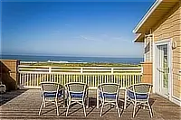 Wooden oceanfront deck with four outdoor chairs, white railing, and panoramic Pacific Ocean views.