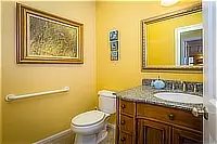 Yellow bathroom with wooden vanity, granite countertop, framed mirror, and toilet.